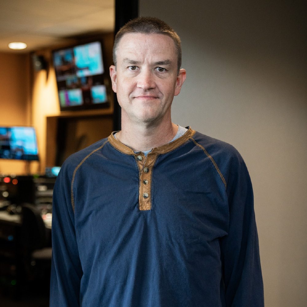 A man in blue shirt standing next to television.