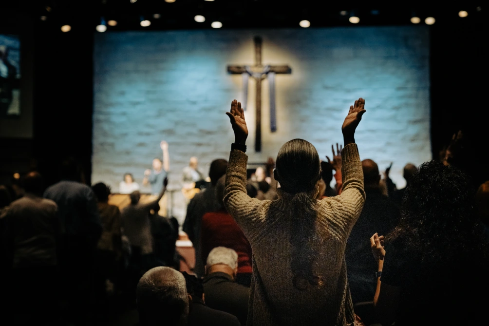 A person with their hands raised in front of a cross.