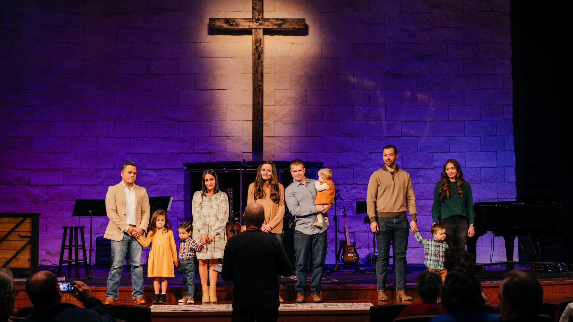 A group of people standing on stage with a cross in the background.