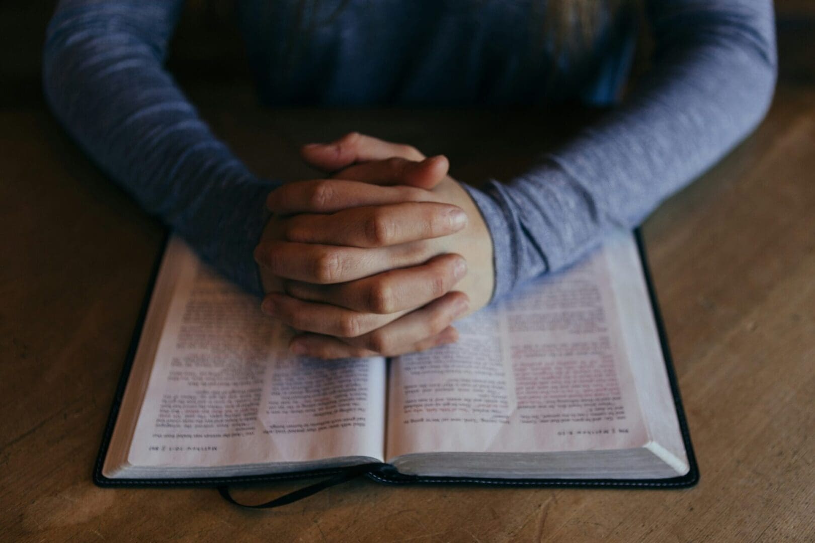 A person is praying on top of an open bible.