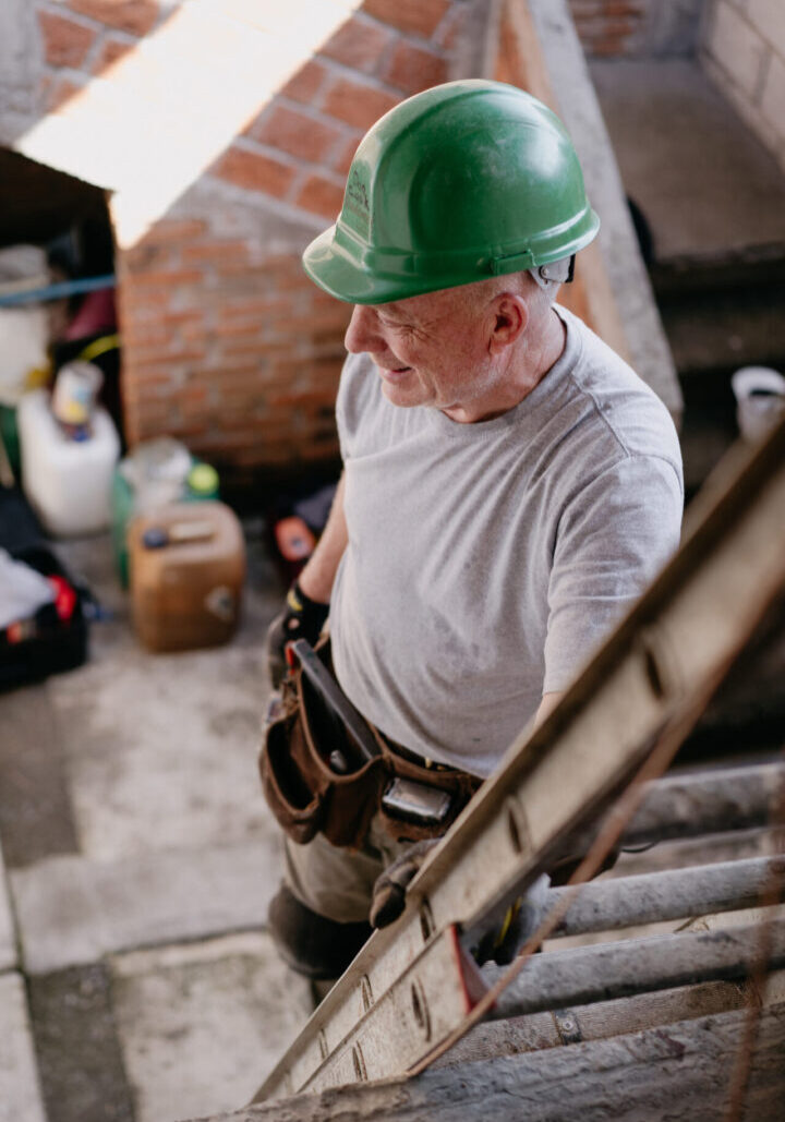A man in green hard hat and gloves standing on stairs.